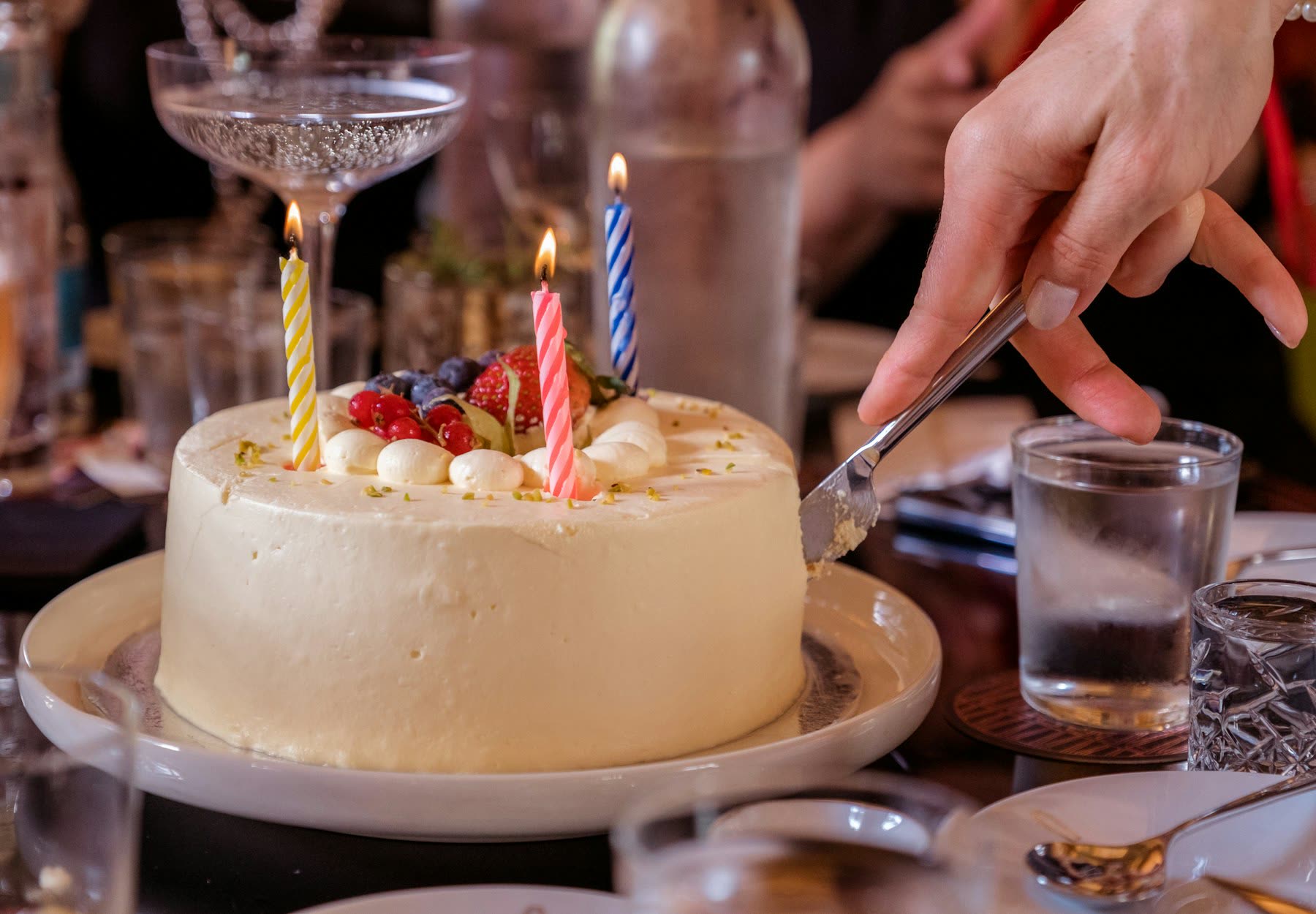 A candle-lit celebration cake being cut at a table